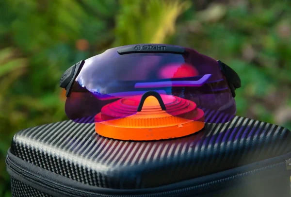 X Sight Sport 2RX shooting glasses with a purple lens color rest on top of an orange clay target, showcasing the lens's impact on contrast and color enhancement. The purple lens effectively darkens the green background, enhancing the visibility of the clay target. This image highlights how the lens color choice can optimize target visibility and improve shooting performance. The glasses' case serves as a reminder of the convenient and protective storage solution provided by X Sight Sport. Experience the difference in clarity and contrast with X Sight Sport shooting glasses.