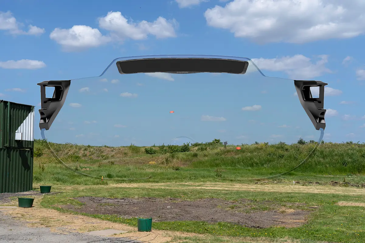 Montage capturing a skeet shooting layout at a shooting ground with a green grass bank at the back and blue skies dotted with clouds in the background. there are two orange clay targets flying across the scene. Superimposed on top is the X Sight lens from behind, providing a visual representation of how the targets and the surroundings appears through the lens color. In this case the lens colour being represented is Clear.