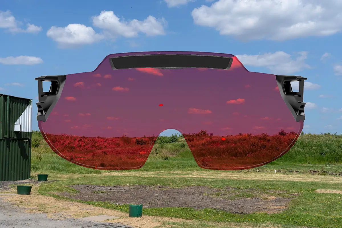 Montage capturing a skeet shooting layout at a shooting ground with a green grass bank at the back and blue skies dotted with clouds in the background. there are two orange clay targets flying across the scene. Superimposed on top is the X Sight lens from behind, providing a visual representation of how the targets and the surroundings appears through the lens color. In this case the lens colour being represented is Dark Crimson.