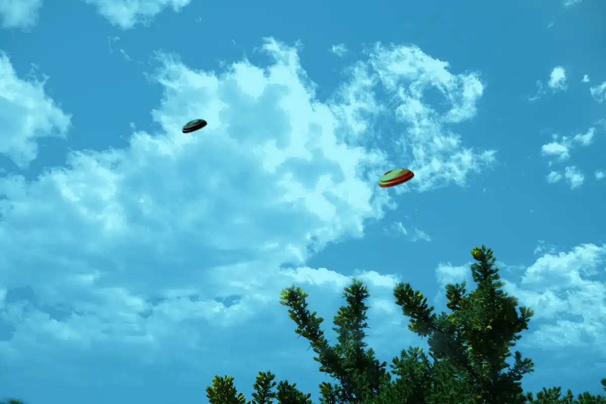 The image shows how the following scene would look when viewed through the Ice Blue lens from X Sight Sport shooting glasses. The scene shows an orange and a black clay target being thrown into the blue sky with clouds.