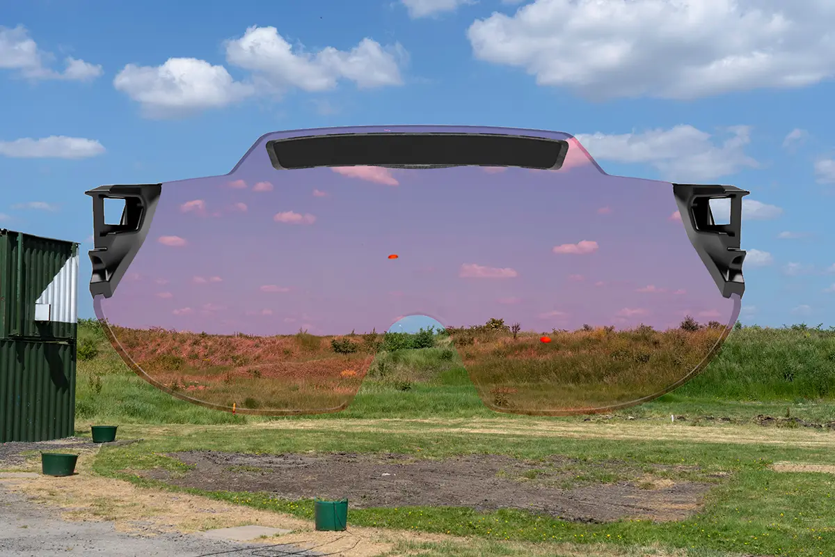 Montage capturing a skeet shooting layout at a shooting ground with a green grass bank at the back and blue skies dotted with clouds in the background. there are two orange clay targets flying across the scene. Superimposed on top is the X Sight lens from behind, providing a visual representation of how the targets and the surroundings appears through the lens color. In this case the lens colour being represented is Light Orange.