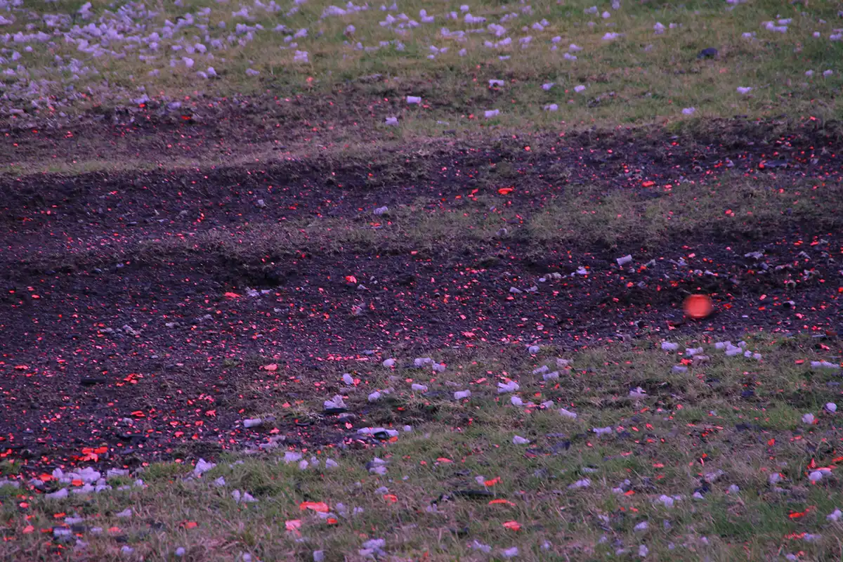 Image shows how the following scene would look when viewed through a light purple lens colour from X Sight Sport. The scene shows an orange rabbit clay target rolling across a dirt grass bank surrounded by wads and orange clay fragments.