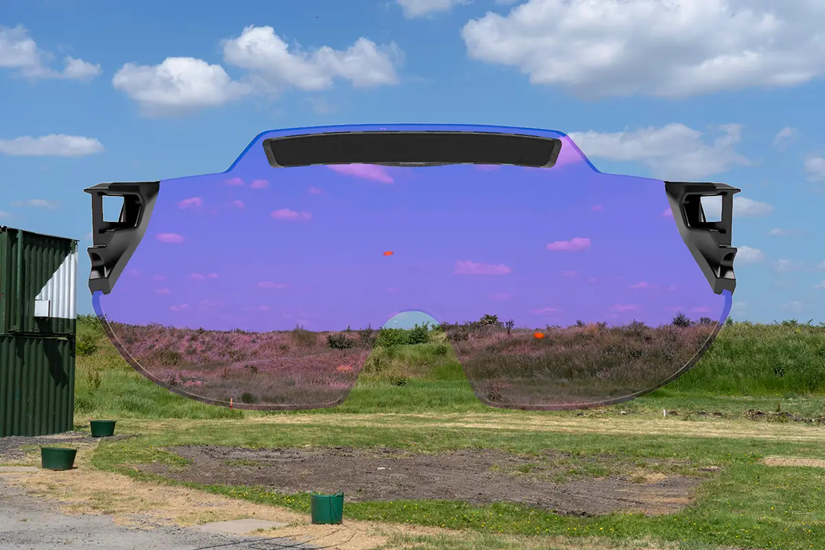 Montage capturing a skeet shooting layout at a shooting ground with a green grass bank at the back and blue skies dotted with clouds in the background. there are two orange clay targets flying across the scene. Superimposed on top is the X Sight lens from behind, providing a visual representation of how the targets and the surroundings appears through the lens color. In this case the lens colour being represented is Light Purple.