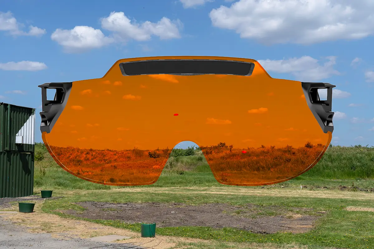 Montage capturing a skeet shooting layout at a shooting ground with a green grass bank at the back and blue skies dotted with clouds in the background. there are two orange clay targets flying across the scene. Superimposed on top is the X Sight lens from behind, providing a visual representation of how the targets and the surroundings appears through the lens color. In this case the lens colour being represented is XTRM orange.