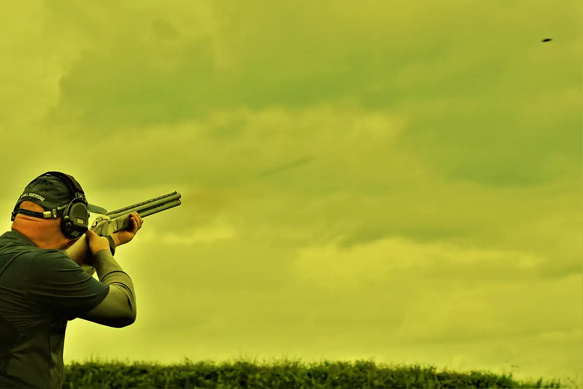 This image shows how the following scene would look when viewed through the XTRM Yellow colour of lens when wearing X Sight Sport shotoing glasses. The scene displays a clay shooter from behind, aiming and shooting at a black clay target in the sky. The trajectory of the shot is visible, highlighting the precision of clay shooting.